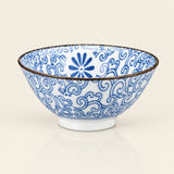 A white ceramic bowl decorated with blue hand-painted floral and scroll patterns, featuring a thin dark rim and a small white footed base, set against a plain off-white background.