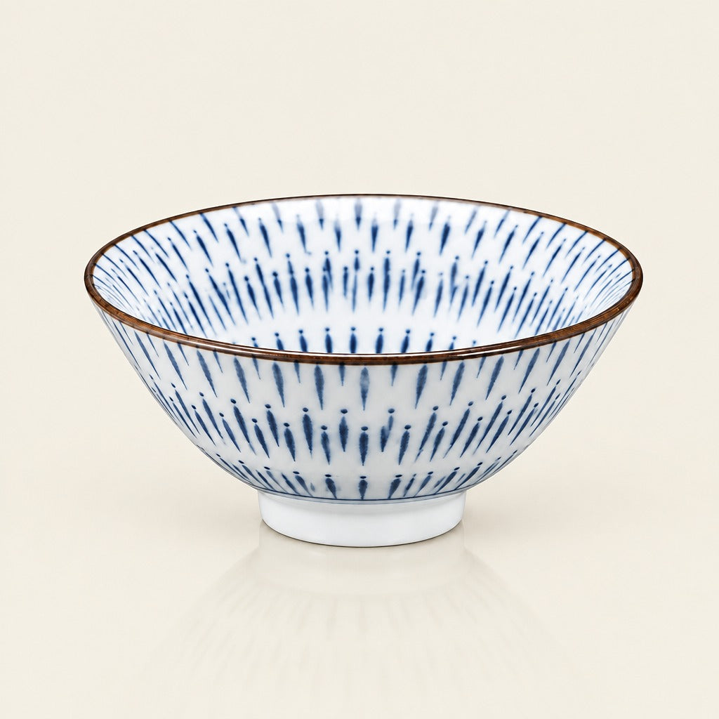 A white ceramic bowl with a blue radial dash pattern and a thin brown rim, shown on a light cream background.