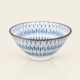 A white ceramic bowl with a blue radial dash pattern and a thin brown rim, shown on a light cream background.