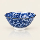 A blue and white patterned ceramic bowl with a black rim, shown on a clean off-white background with a soft reflection underneath.