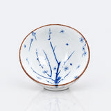 A white ceramic bowl decorated with blue floral and bird motifs and a thin brown rim, photographed on a clean white background.