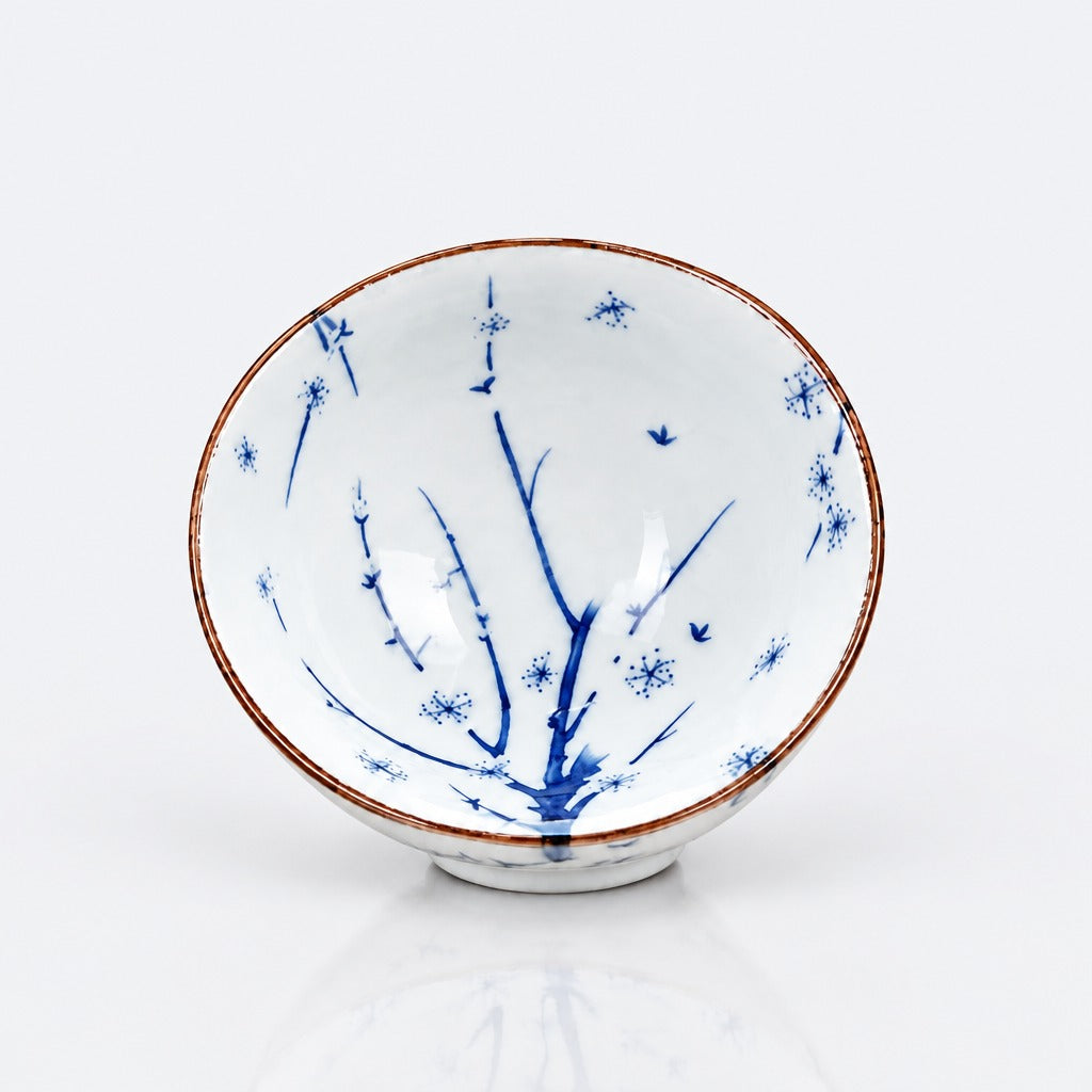 A white ceramic bowl decorated with blue floral and bird motifs and a thin brown rim, photographed on a clean white background.