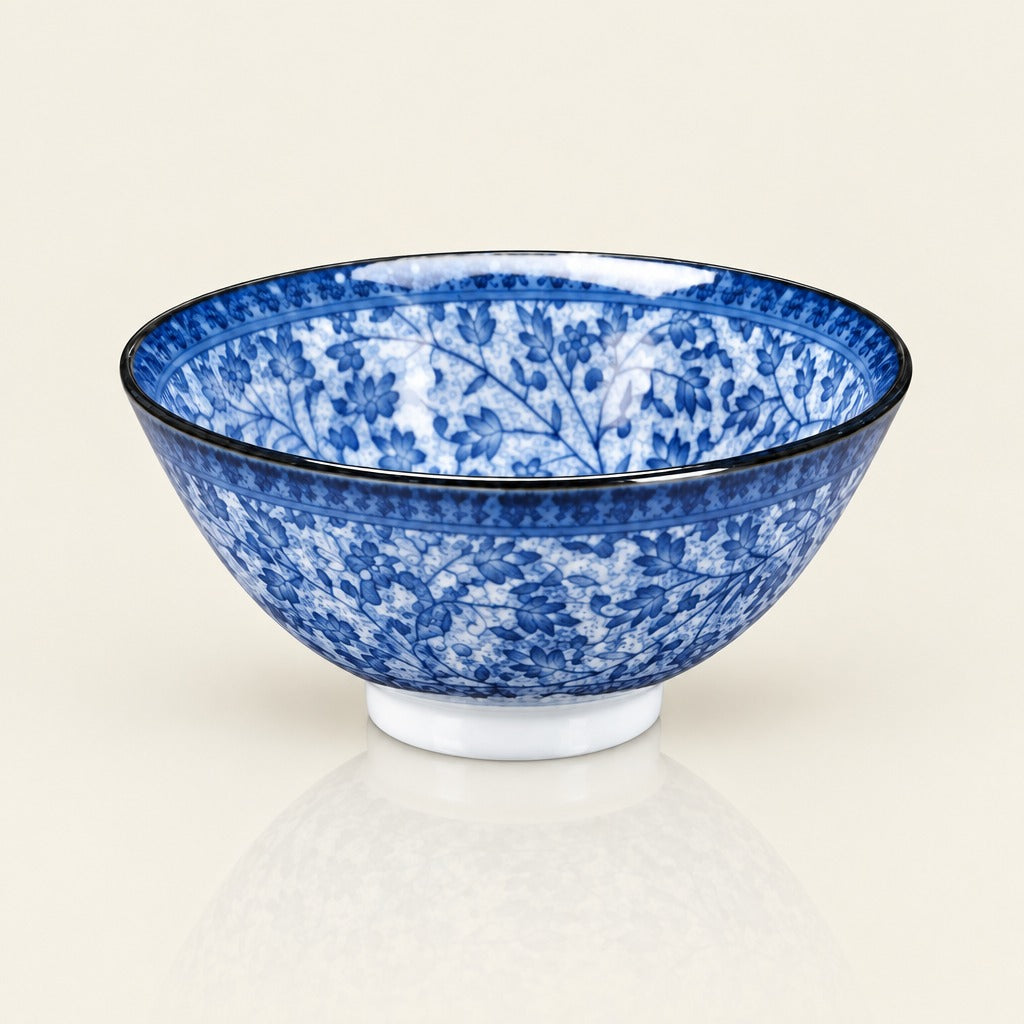 A blue and white floral pattern ceramic bowl with a black rim, displayed on a clean, light beige reflective surface.