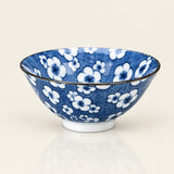 A blue and white floral patterned ceramic bowl with a dark rim, displayed on a clean, light beige reflective surface.