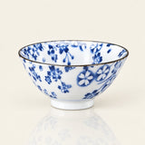 A white ceramic bowl decorated with a blue floral pattern and a thin dark rim, shown on a clean off-white background with a soft reflection below.