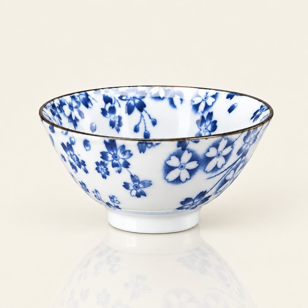 A white ceramic bowl decorated with a blue floral pattern and a thin dark rim, shown on a clean off-white background with a soft reflection below.
