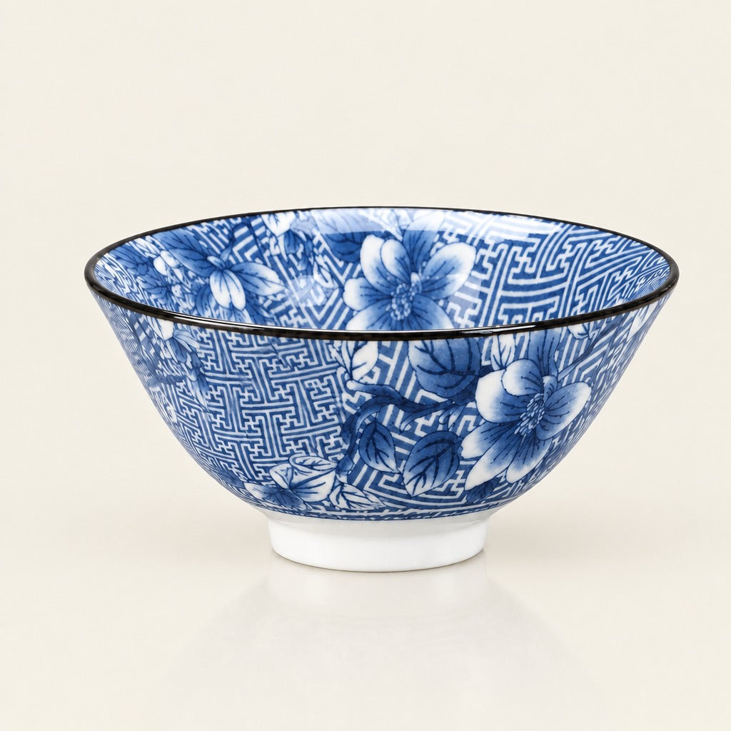 A blue and white ceramic bowl with a floral and geometric pattern, featuring a black rim and a white base, photographed on a clean off-white background.