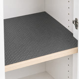 A dark gray textured shelf liner with a raised geometric pattern, shown installed on a wooden shelf inside a white storage cabinet.