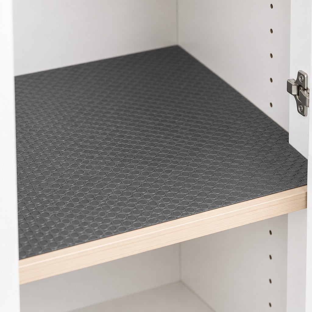 A dark gray textured shelf liner with a raised geometric pattern, shown installed on a wooden shelf inside a white storage cabinet.