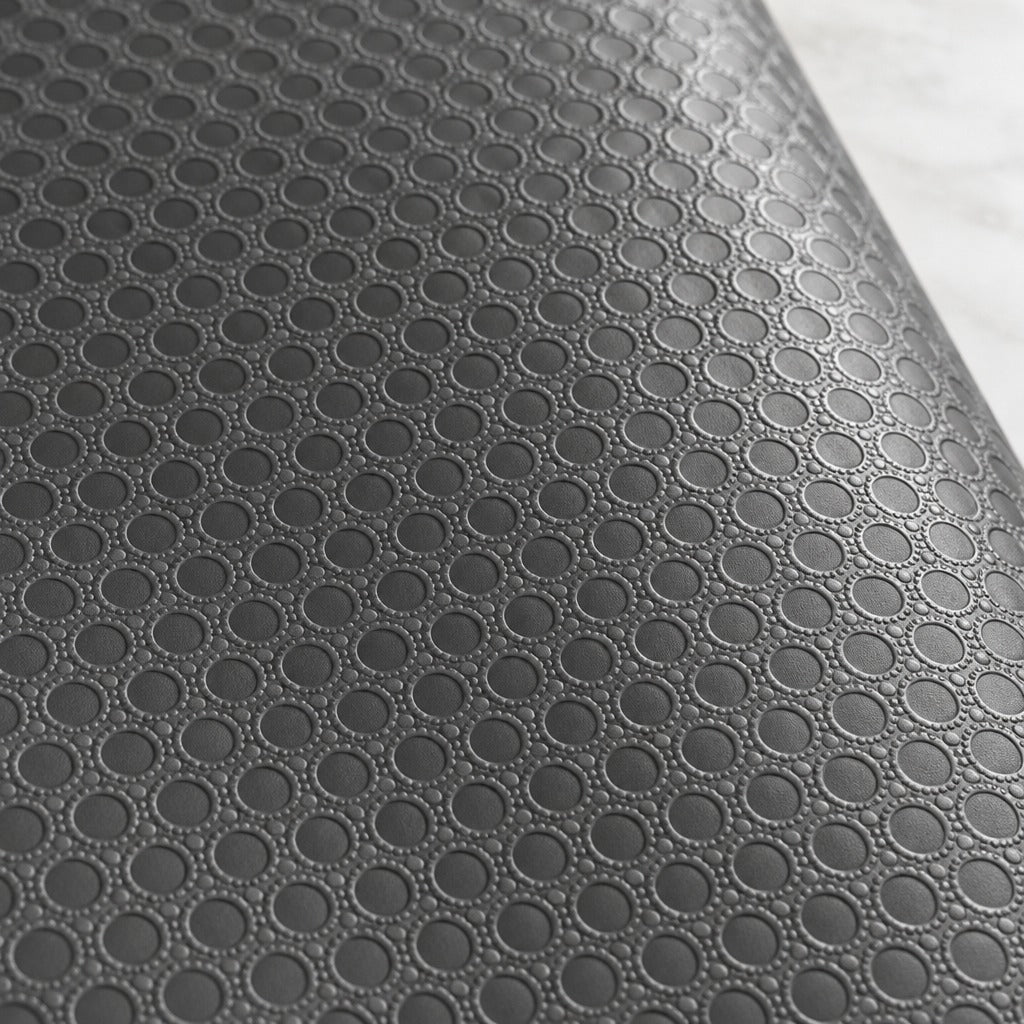 A close-up of a dark gray textured surface with a repeating circular embossed pattern, shown against a light marble-like background.