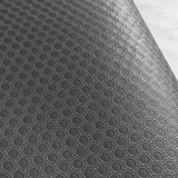 A close-up of a dark gray textured surface with a repeating circular embossed pattern, shown against a light marble-like background.