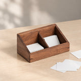 A rectangular wooden desk organizer with two angled compartments, shown holding white cards on a light wood tabletop with a few cards placed beside it.