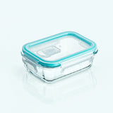 A rectangular clear glass food storage container with a translucent aqua blue silicone seal and lid, shown on a clean white background with a soft reflection.