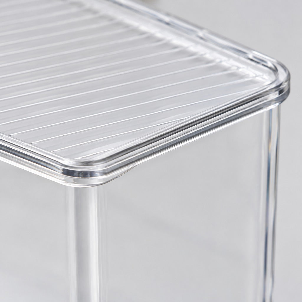 Close-up of a transparent acrylic side table with a slatted top and clear legs on a light gray background.