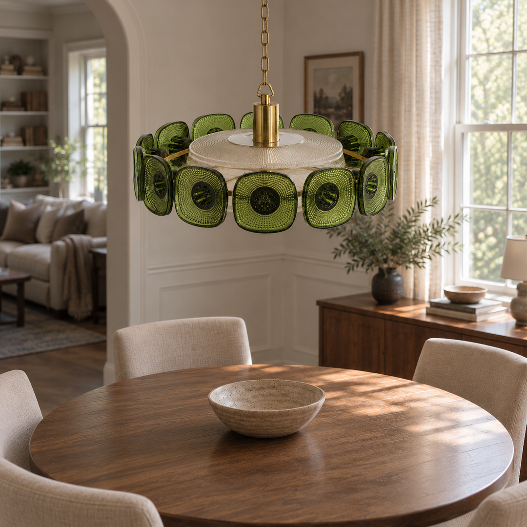 A modern circular pendant chandelier with green textured glass discs and a brass center, hanging over a round wooden dining table in a bright, modern dining room.