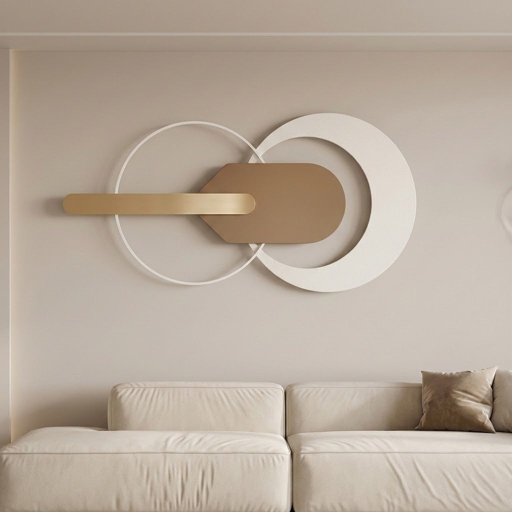 Modern wall-mounted abstract decor piece with interlocking white and tan geometric shapes and a horizontal gold bar, displayed above a light beige sofa in a minimalist living room.