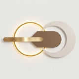 Modern wall sconce with a glowing gold ring, a horizontal brushed gold bar, a brown geometric center piece, and a large white crescent-shaped overlay, shown against a plain light background.