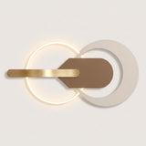 Modern wall sconce with a glowing circular ring, a horizontal brushed gold bar, and overlapping matte white and brown geometric shapes on a light neutral background.