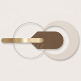 Abstract geometric wall art featuring a horizontal brushed gold bar, a brown rounded rectangle, and overlapping translucent white circular rings on a light beige background.