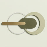 A minimalist geometric wall light fixture with overlapping circular and curved metal elements in beige, olive green, and brushed gold, shown against a solid off-white background.