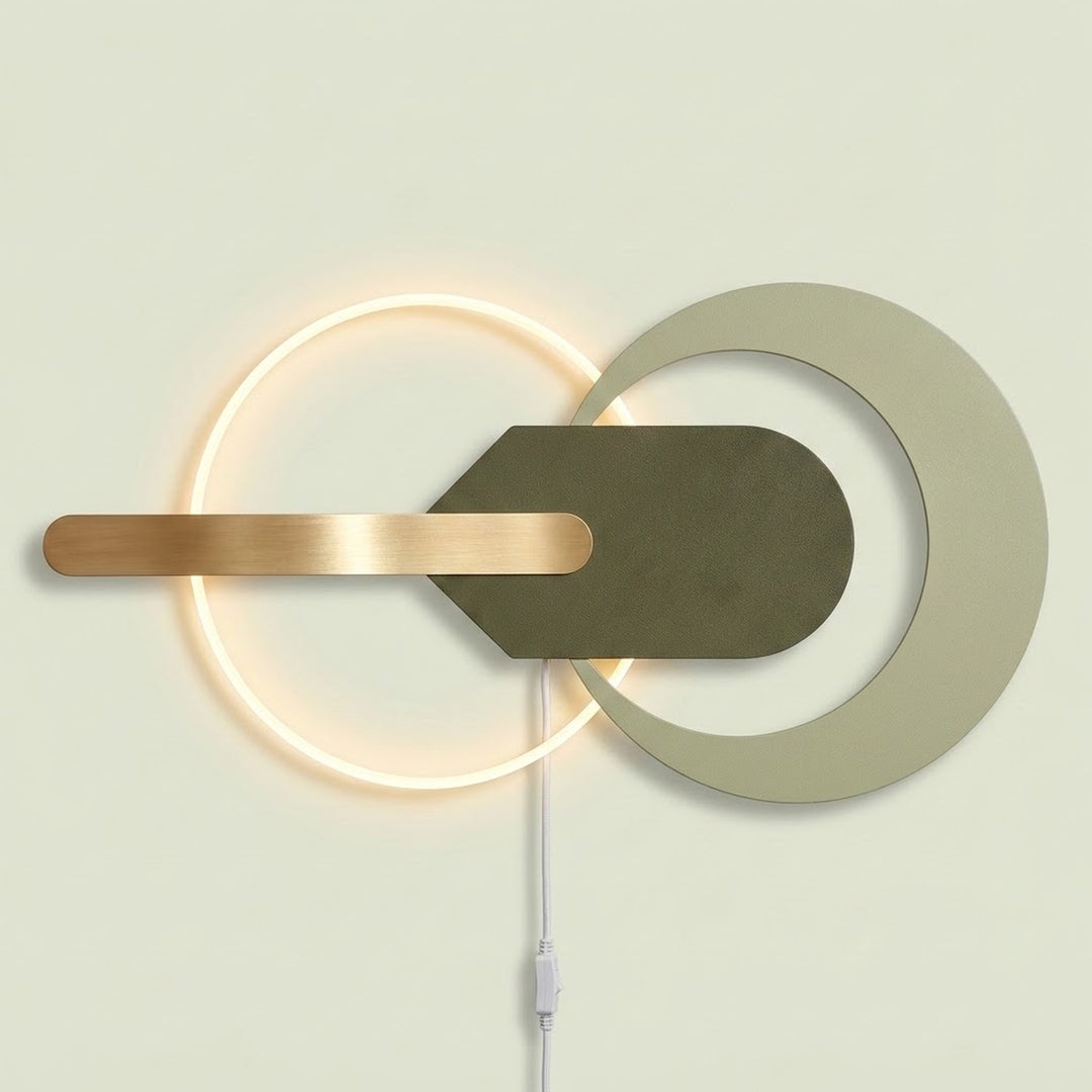 Modern wall-mounted light fixture with a glowing circular ring, a large matte off-white circular cutout, a dark olive green geometric center, and a horizontal brushed brass bar, shown against a pale beige wall.