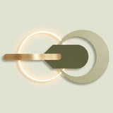Modern wall sconce with a glowing circular ring, a matte olive green arrowhead shape, and a brushed brass bar on a light beige background.
