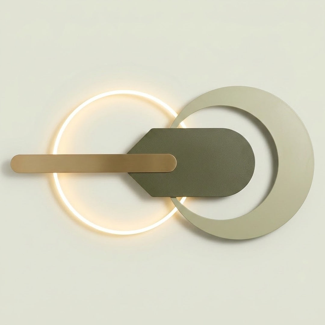 Modern wall sconce with a glowing circular ring, a horizontal brushed brass bar, and a dark gray geometric shield overlay on a light beige background.