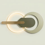Modern wall sconce with a glowing circular ring, a horizontal brushed brass bar, and a dark gray geometric shield overlay on a light beige background.