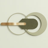 Modern wall-mounted light fixture with overlapping circular and curved metal elements in matte gray, olive green, and brushed gold, shown against a plain off-white wall.