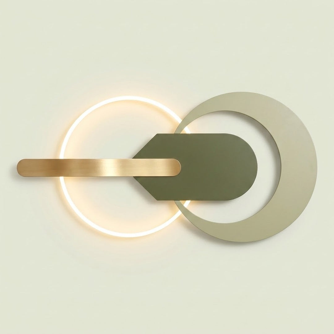Modern wall sconce with a glowing circular ring, a horizontal brushed gold bar, and a central dark olive green shield shape layered over a large pale beige ring on a light warm background.