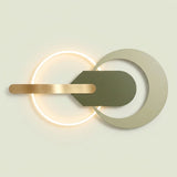 Modern wall sconce with a glowing circular ring, a horizontal brushed gold bar, and a central dark olive green shield shape layered over a large pale beige ring on a light warm background.