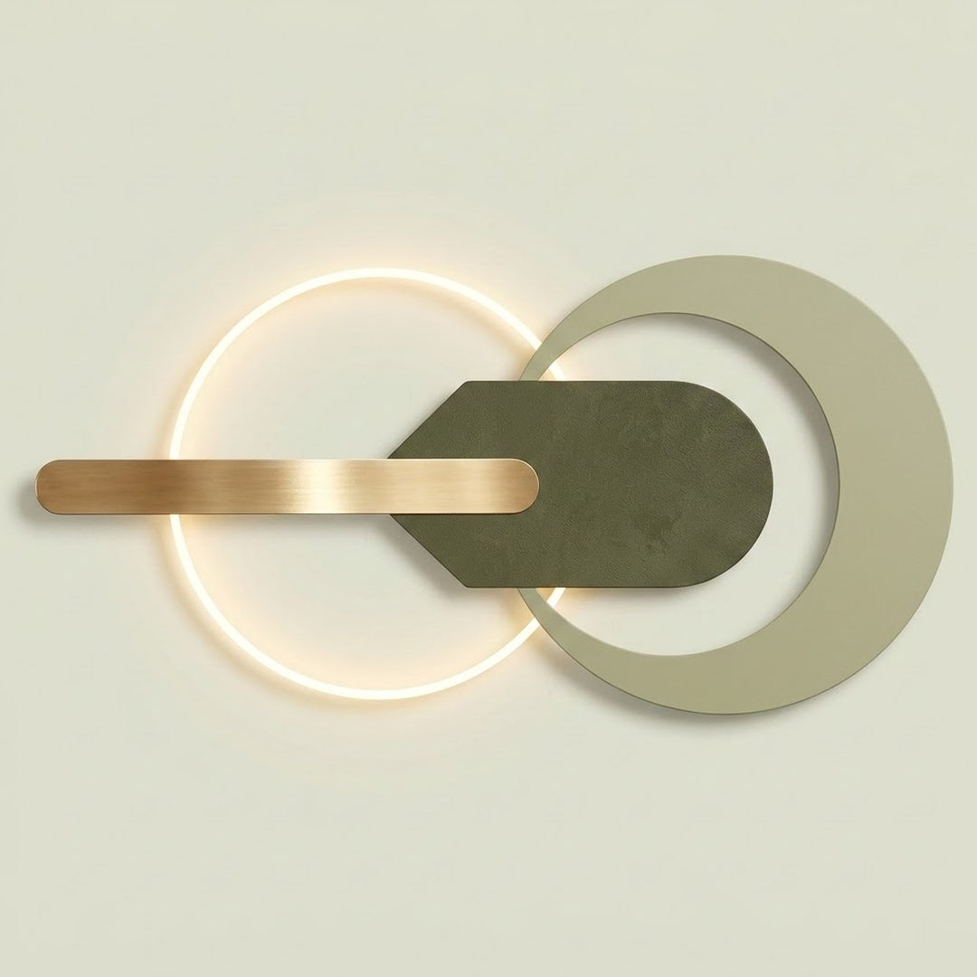 Modern wall-mounted light fixture with a glowing circular ring, a matte olive green geometric central element, and a brushed brass horizontal bar on a light beige background.