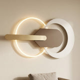 Modern wall-mounted light fixture with two circular rings, one illuminated in warm white, a white outer ring, a matte taupe central panel, and a brushed gold horizontal bar, shown mounted on a beige wall above a sofa.
