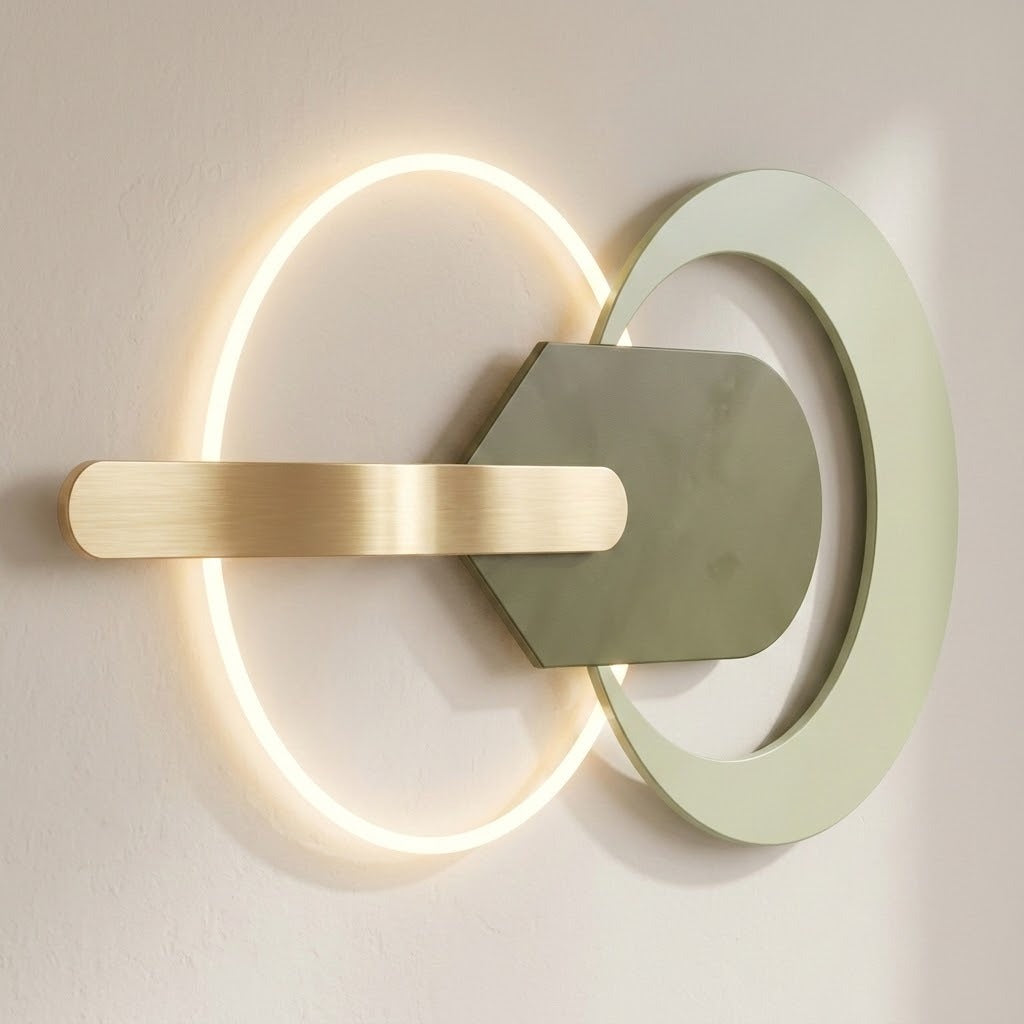 Wall light with a glowing warm-white ring, sage-green circular frame and central plate, and horizontal gold-tone bar against a beige wall.