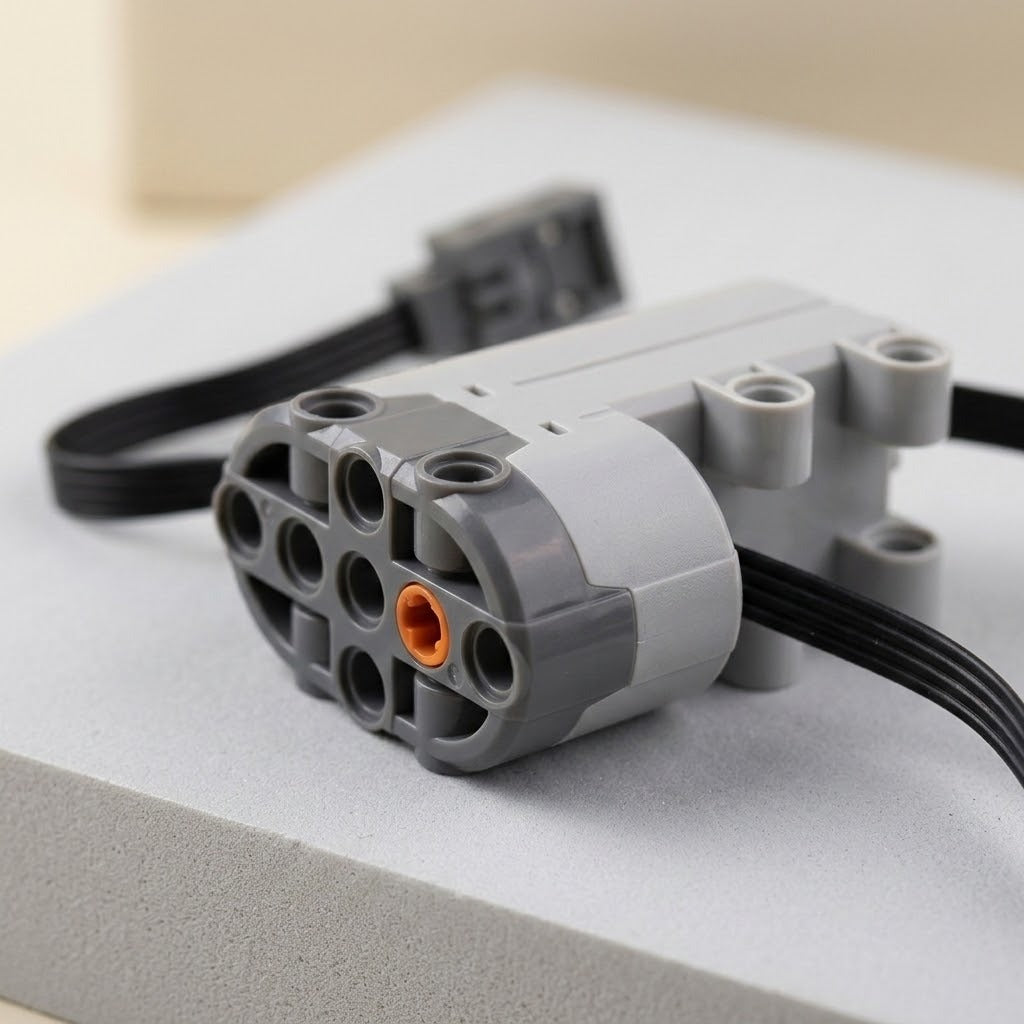 A grey plastic building block motor component with orange axle socket and black cable rests on a pale raised surface.