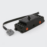 A black building block train motor component with orange axle sockets, a black cable, and a gray connector rests against a white background.