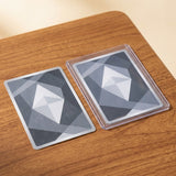 Two rectangular cards with a gray and white geometric faceted gem design, one resting flat and the other inside a clear protective sleeve, placed on a wooden tabletop.