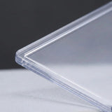 A close-up of a transparent hard card sleeve shows its rounded corner, layered edge, and smooth surface.
