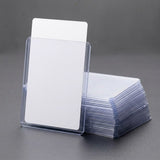 A clear plastic card sleeve holding blank white cards, with a stack of similar sleeves and cards on a dark gray surface.