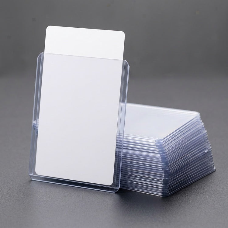 A clear plastic card sleeve holding blank white cards, with a stack of similar sleeves and cards on a dark gray surface.