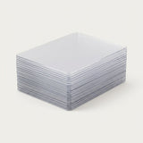 Clear plastic card sleeves are stacked neatly on a plain off-white background, showing their rigid edges and rounded corners.