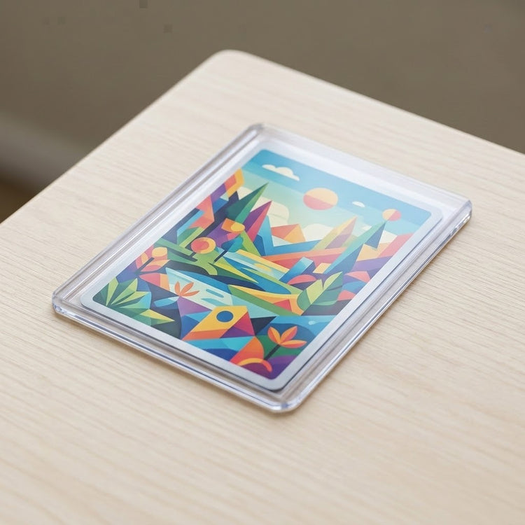 A transparent hard card sleeve holds a colorful geometric art card on a light wood tabletop.