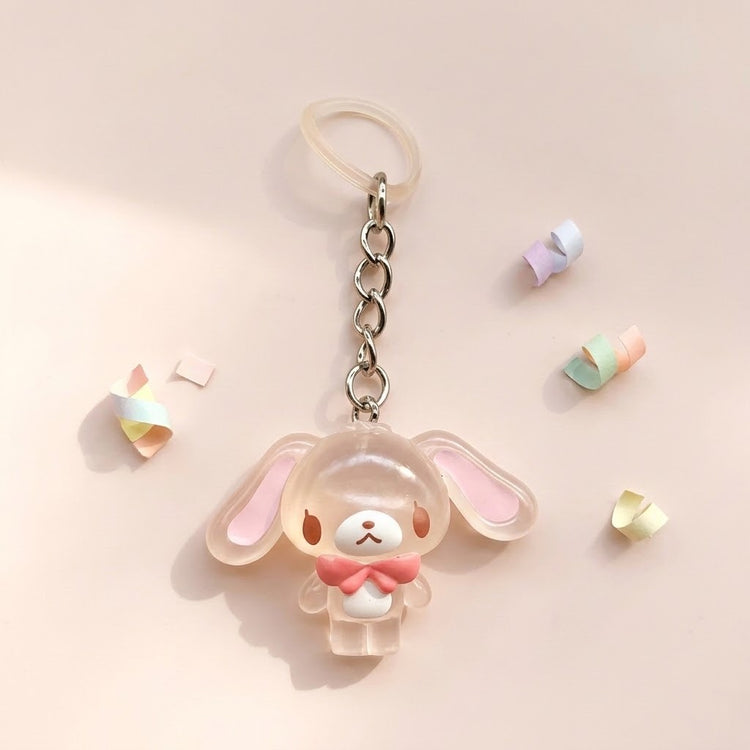 A cute translucent acrylic keychain charm shaped like a bunny with long floppy ears, a white face, and a pink bow tie, attached to a silver chain and clear ring on a soft beige background.