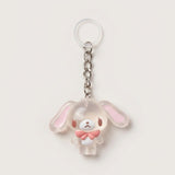 A cute bunny-shaped keychain charm made of translucent frosted acrylic with pink inner ears and a pink bow tie, attached to a silver metal chain and clear plastic key ring on a light beige background.