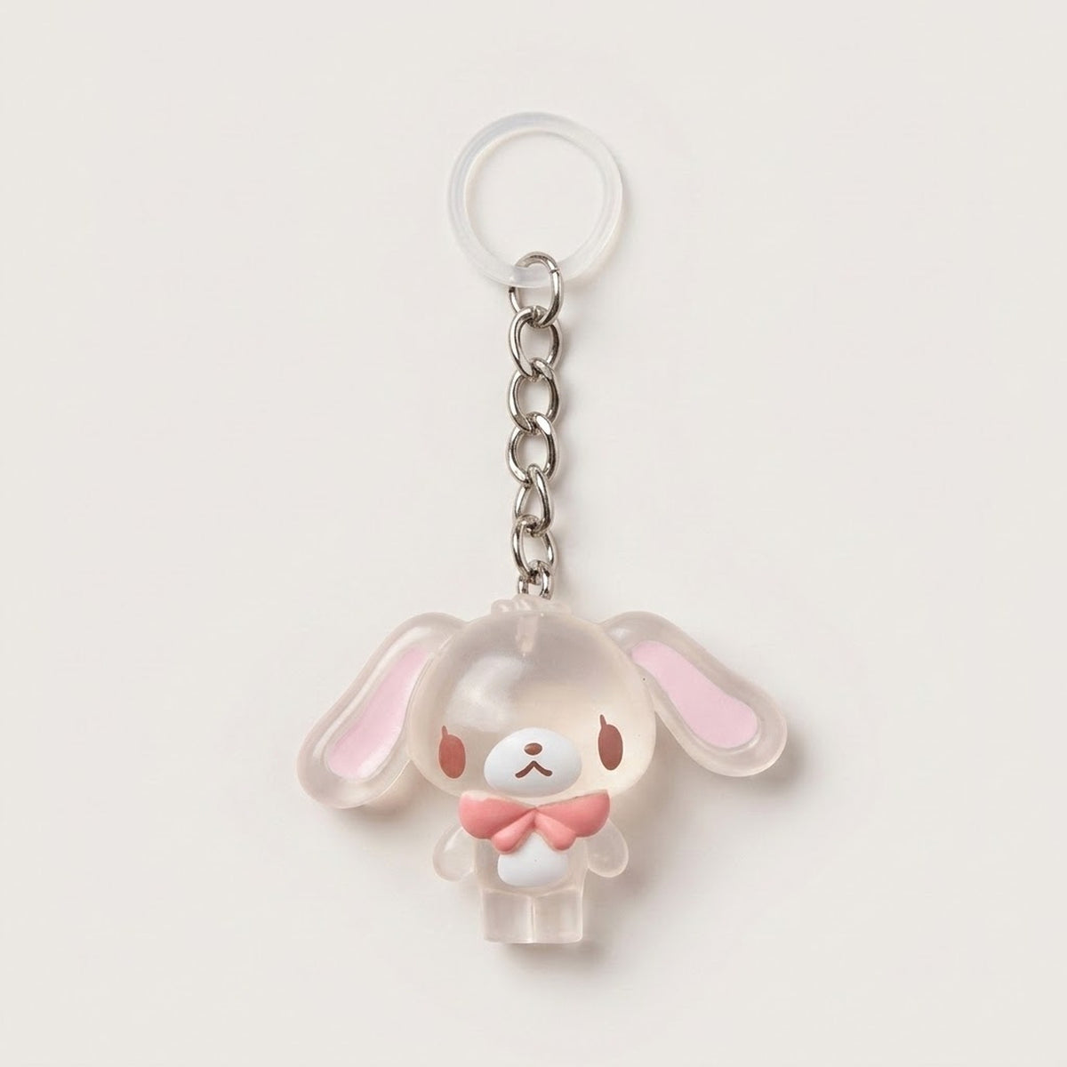 A cute bunny-shaped keychain charm made of translucent frosted acrylic with pink inner ears and a pink bow tie, attached to a silver metal chain and clear plastic key ring on a light beige background.