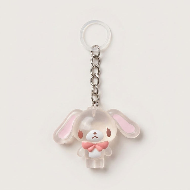A cute bunny-shaped keychain charm made of translucent frosted acrylic with pink inner ears and a pink bow tie, attached to a silver metal chain and clear plastic key ring on a light beige background.