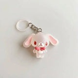 A cute, small white cartoon bunny keychain charm with pink inner ears, red eyes, and a pink bow, attached to a silver metal split ring on a light gray background.
