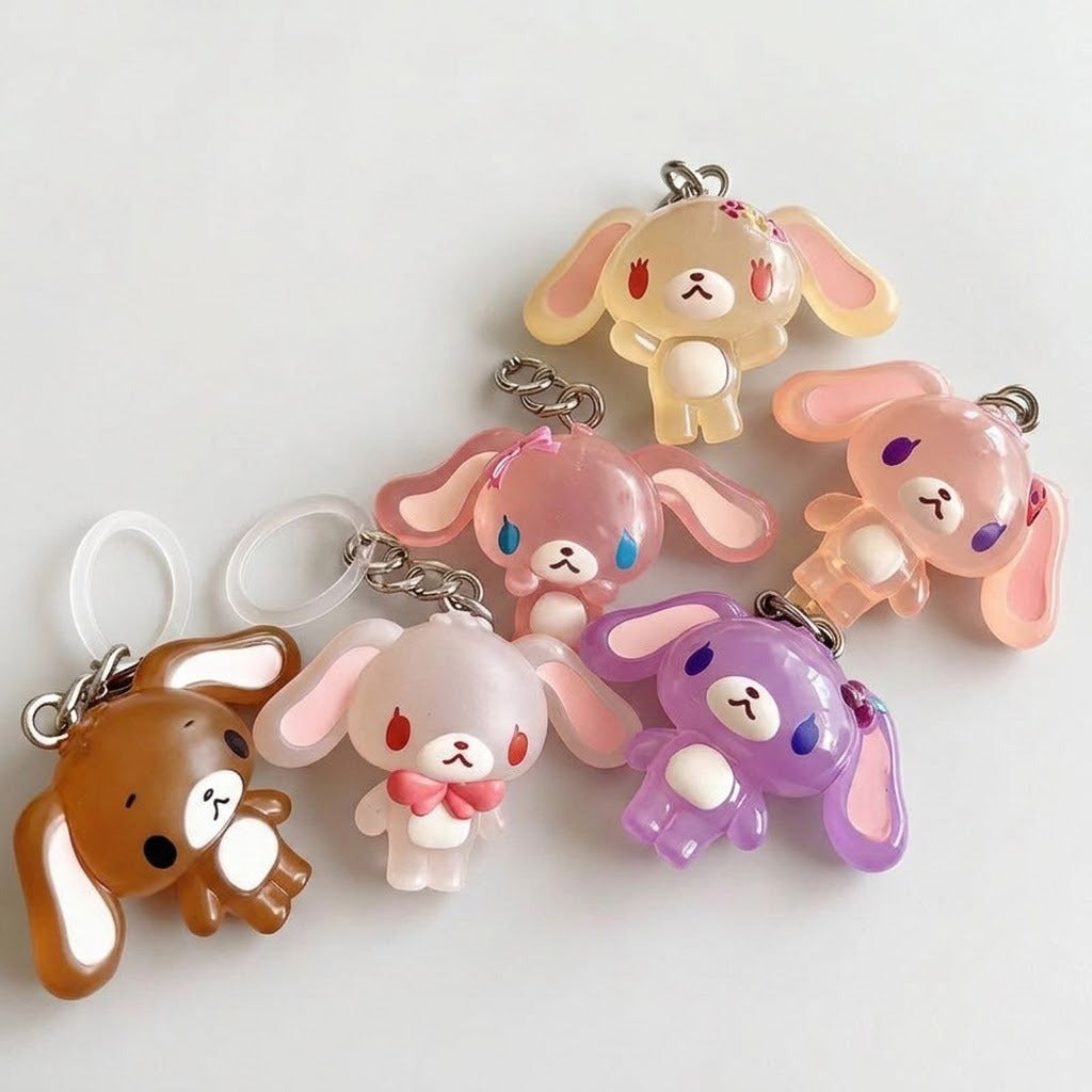 Five translucent rabbit-shaped keychains in different colors, including brown, pink, cream, purple, and white, arranged on a plain light background.