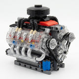 A plastic V8 engine model kit with transparent housings, black hoses, and a red top panel on a plain white background.