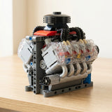 Assembled plastic V8 engine model kit with clear cylinder covers, gray pipes, and red accents sits on a light wood tabletop.